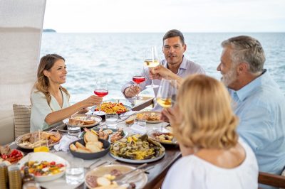 Happy family toasting wine glasses while having lunch on luxury yacht.